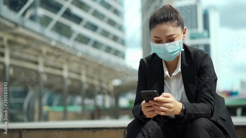 business woman using smartphone and wearing medical mask for protection from coronavirus (covid-19) pandemic in the city photo