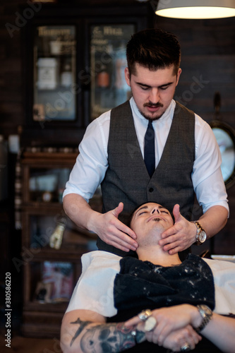 A gentleman barber applies a soothing skin lotion to a client after a shave. photo