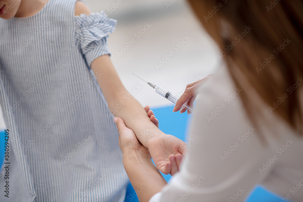 Doctor holding the syringe with vaccine and taking girls hand Doctor holding the syringe with vaccine and taking girls hand