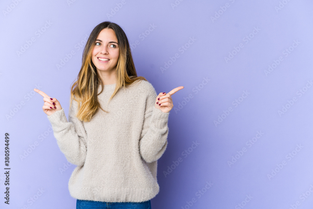 Young caucasian woman isolated on purple background pointing to different copy spaces, choosing one of them, showing with finger. Young caucasian woman isolated on purple background pointing to different copy spaces, choosing one of them, showing with finger.