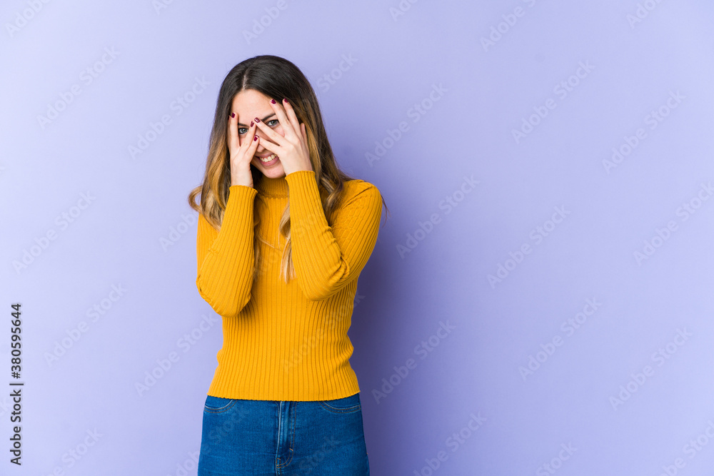 Young caucasian woman isolated on purple background blink at the camera through fingers, embarrassed covering face. Young caucasian woman isolated on purple background blink at the camera through fingers, embarrassed covering face.