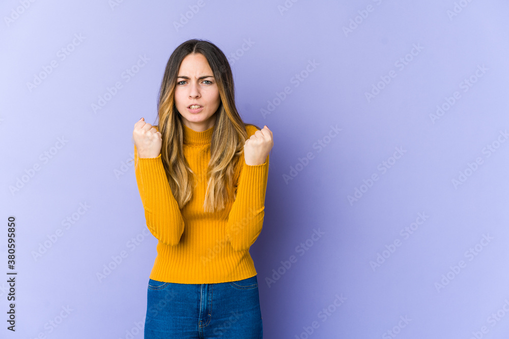 Young caucasian woman isolated on purple background showing fist to camera, aggressive facial expression. Young caucasian woman isolated on purple background showing fist to camera, aggressive facial expression.