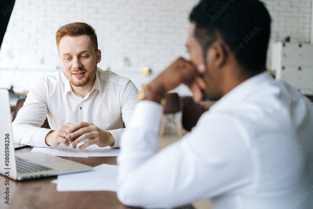 Handsome happy young business man explaining to African partner the benefits of new deal to colleague or client. Businessman holding conversation with business client. Handsome happy young business man explaining to African partner the benefits of new deal to colleague or client. Businessman holding conversation with business client.
