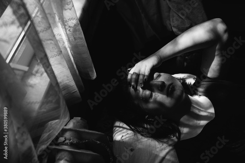 Beautiful woman raises her hand to her face while lying on a bed below a curtain.