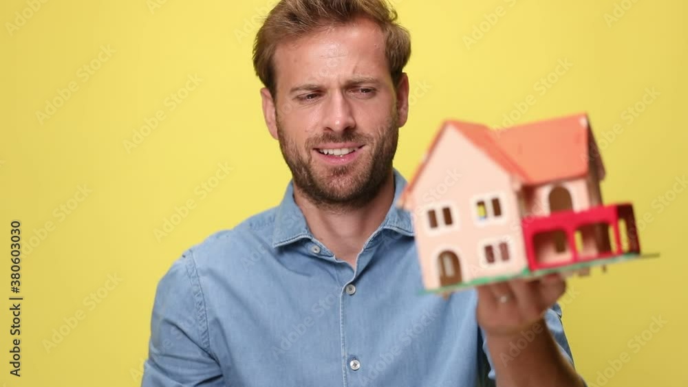 businessman showing a house model and celebrating succes on yellow background businessman showing a house model and celebrating succes on yellow background