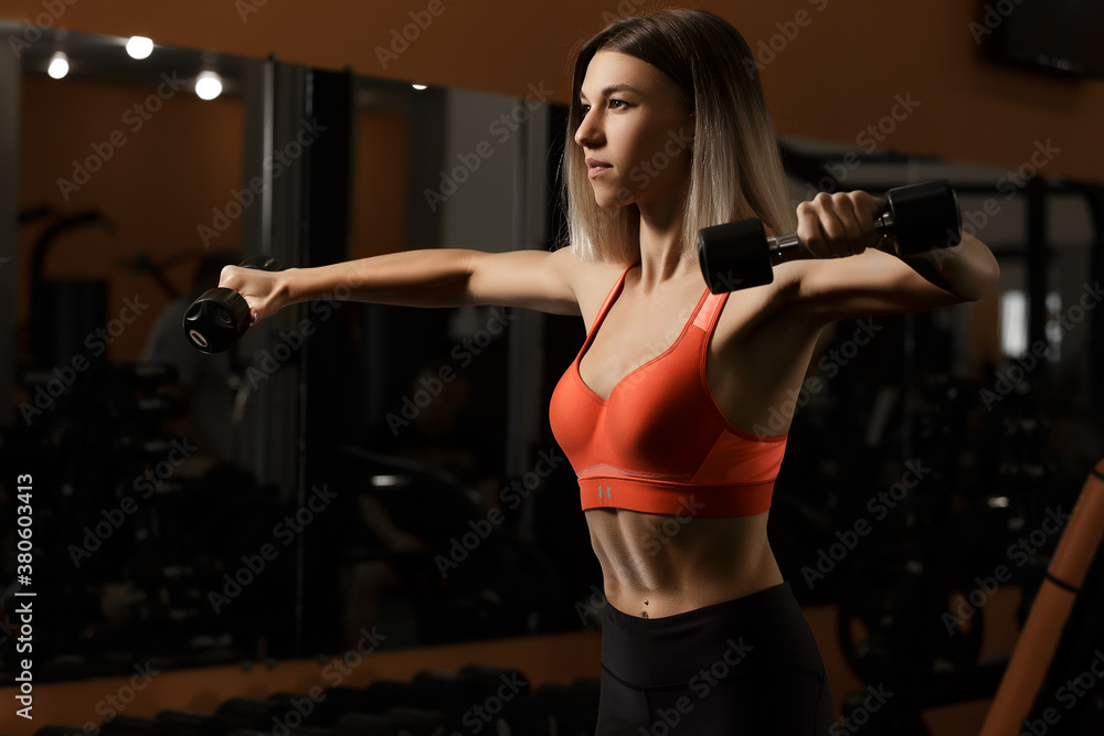 Gorgeous blonde lifts weights and trains biceps in the gym. A woman with dumbbells is working on her figure. The girl has a good body shape and abdominal muscles. Fitness sport concept. Gorgeous blonde lifts weights and trains biceps in the gym. A woman with dumbbells is working on her figure. The girl has a good body shape and abdominal muscles. Fitness sport concept.