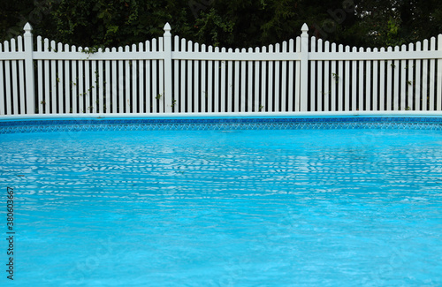 Swimming pool and white vinyl fence in front of trees