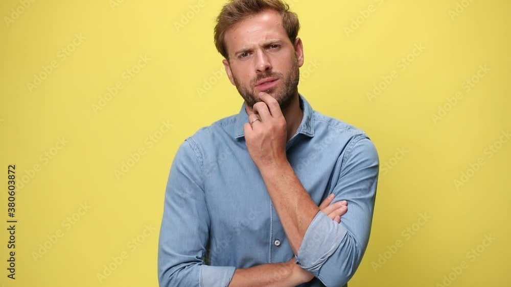 attractive businessman standing with his arms crossed, touching his face and thinking of something but couldn't figure out the answer on yellow background attractive businessman standing with his arms crossed, touching his face and thinking of something but couldn't figure out the answer on yellow background