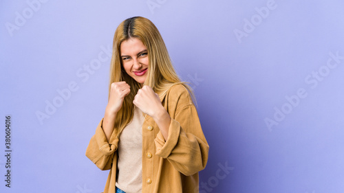 Young blonde woman isolated on purple background showing fist to camera, aggressive facial expression.