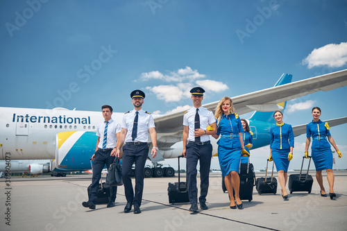 Cheerful pilots and flight attendants carrying travel bags at airport Fototapeta