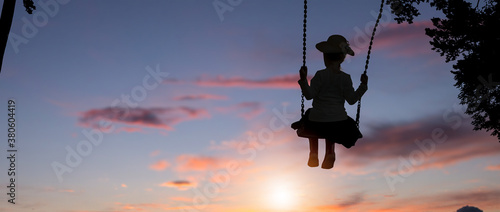 The silhouette of child girl is swing in sunset sky.