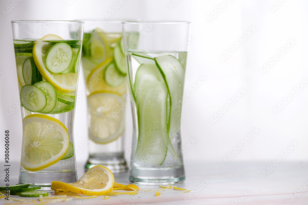 Three glasses of cucumber and lemon refreshing drink decorated with sliced lemon and cucumber on marble table with white background. Three glasses of cucumber and lemon refreshing drink decorated with sliced lemon and cucumber on marble table with white background.