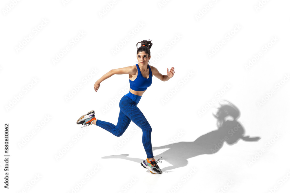 Movement. Beautiful young female athlete practicing on white studio background, portrait with shadows. Sportive fit model in motion and action. Body building, healthy lifestyle, style concept.