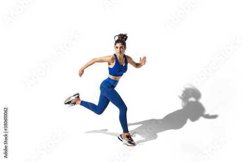 Movement. Beautiful young female athlete practicing on white studio background, portrait with shadows. Sportive fit model in motion and action. Body building, healthy lifestyle, style concept. © master1305