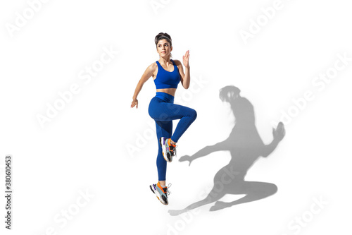 Movement. Beautiful young female athlete practicing on white studio background, portrait with shadows. Sportive fit model in motion and action. Body building, healthy lifestyle, style concept.