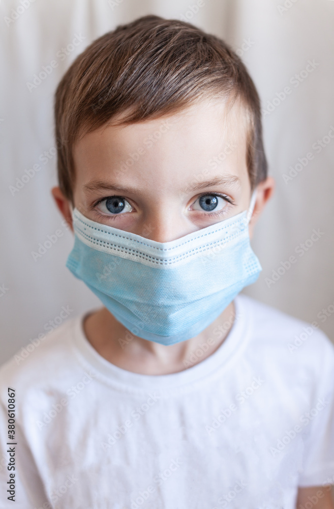 Six-year-old boy on a white background in a white T-shirt with a blue protective mask on his face Six-year-old boy on a white background in a white T-shirt with a blue protective mask on his face