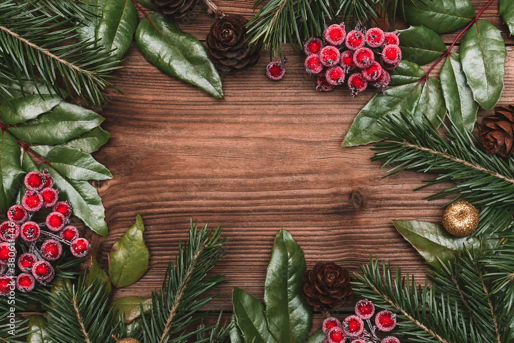 Christmas frame made of fir tree and holly branches,cones,viburnum berries on the dark wooden rustic background.Christmas background.Copy space for text, top view. Christmas frame made of fir tree and holly branches,cones,viburnum berries on the dark wooden rustic background.Christmas background.Copy space for text, top view.