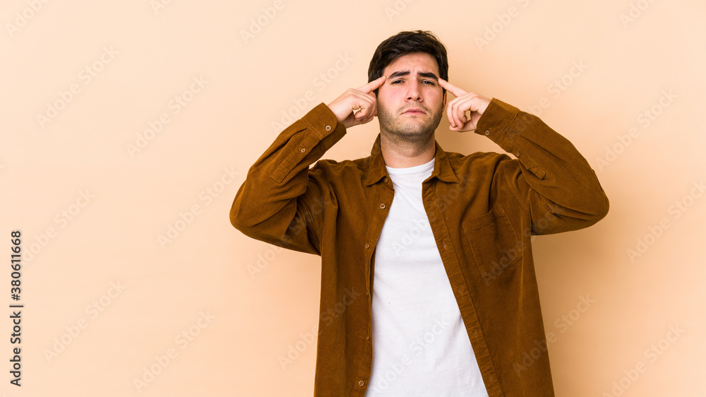 Young man isolated on beige background focused on a task, keeping forefingers pointing head. Young man isolated on beige background focused on a task, keeping forefingers pointing head.