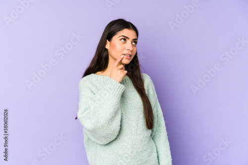 Young indian woman isolated on purple background looking sideways with doubtful and skeptical expression. © Asier