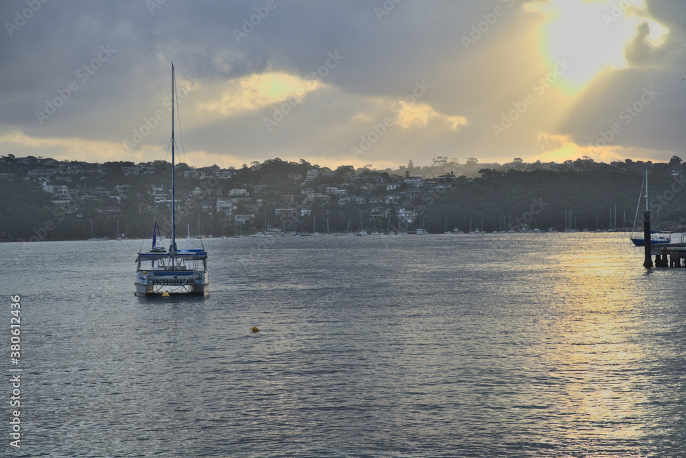 Yacht in water at sunset against a background of Manly cove marine and rural houses, Manly, New South Wales, Australia