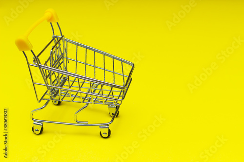 Shopping trolley on bright yellow background, buy and sell concept.