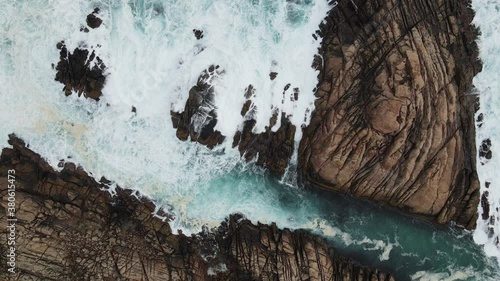 birds eve view flying upwards revealing waves crashing over a large rock formation during a storm.  Along the coastline of Western Australia 4k drone shot.