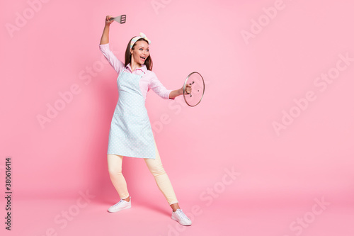 Full length body size view of her she nice attractive cheerful playful housewife holding in hands kitchenware dancing daily routine weekend holiday stay home isolated over pink pastel color background © deagreez