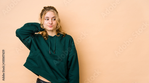 Young caucasian woman isolated on beige background touching back of head, thinking and making a choice. © Asier