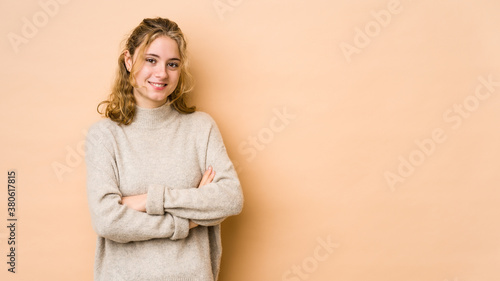 Young caucasian woman isolated on beige background who feels confident  crossing arms with determination.