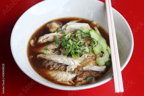 Thai style of chicken noodle with bitter gourd in white bowl on red table background. One of the most popular Thai street food dishes to try