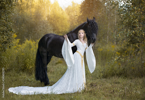 Elven story: blonde elf with a huge black stallion in a sunny forest photo