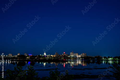 A photo of the Riverfront Park skyline at night seen from across the Susquehanna River at sunset. The buildings reflections are shown in the river. 