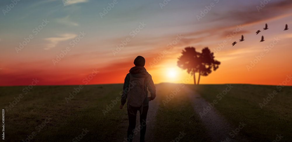 a traveler girl walking along grass way on sunset landscape.