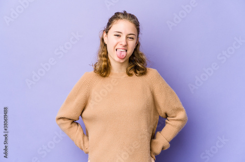 Young caucasian woman on purple background funny and friendly sticking out tongue.