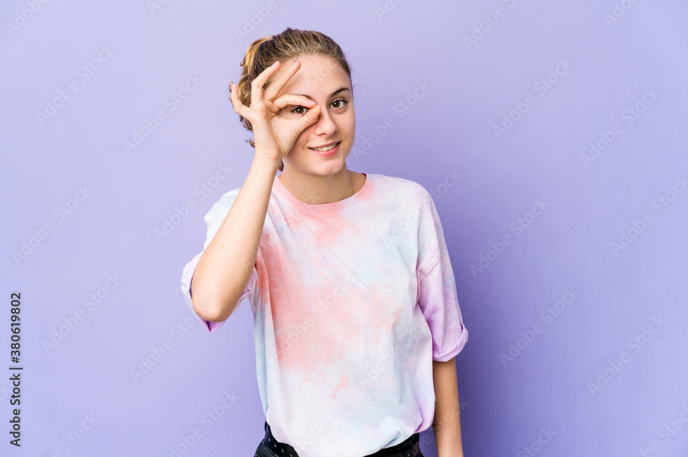 Young caucasian woman on purple background excited keeping ok gesture on eye. Young caucasian woman on purple background excited keeping ok gesture on eye.