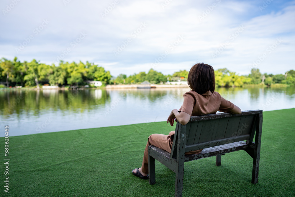 Woman sitting alone on wooden chair near river and green view.