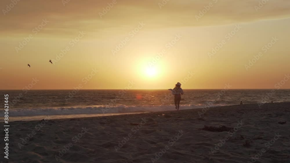 Young Carefree Woman Running on Sandy Beach Under Sunset Sunlight Above Ocean. Healthy Lifestyle and Freedom Concept, Slow Motion Young Carefree Woman Running on Sandy Beach Under Sunset Sunlight Above Ocean. Healthy Lifestyle and Freedom Concept, Slow Motion