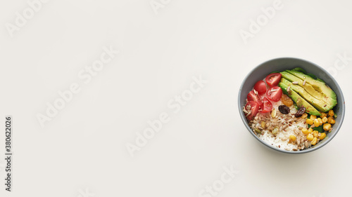 Top view of healthy vegetable bowl lunch with sliced cherry tomatoes, avocado, corn, rice and seeds isolated over white background