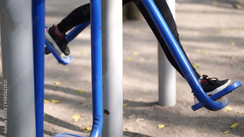 Portrait of woman's legs on street simulator in park. Close up of body part of female doing sports on athletic field in autumn season Portrait of woman's legs on street simulator in park. Close up of body part of female doing sports on athletic field in autumn season