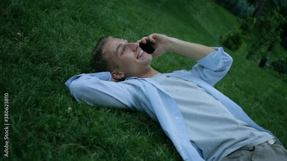delighted man talks on modern black smartphone and lies on green recreational park grass slow motion closeup delighted man talks on modern black smartphone and lies on green recreational park grass slow motion closeup