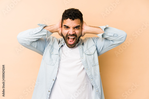 Young mixed race arabic man isolated covering ears with hands trying not to hear too loud sound. © Asier