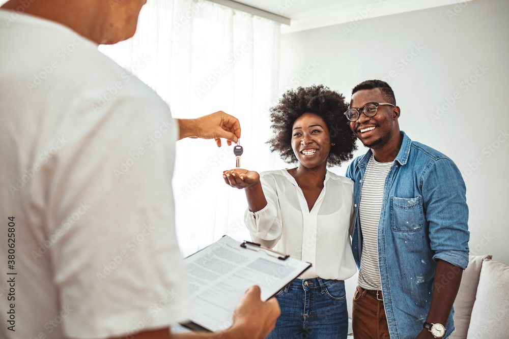 Obraz premium Handsome realtor is giving key to the new apartment to happy young couple. Couple buying new apartment. A young couple receive the keys to their new apartment from a letting agent.