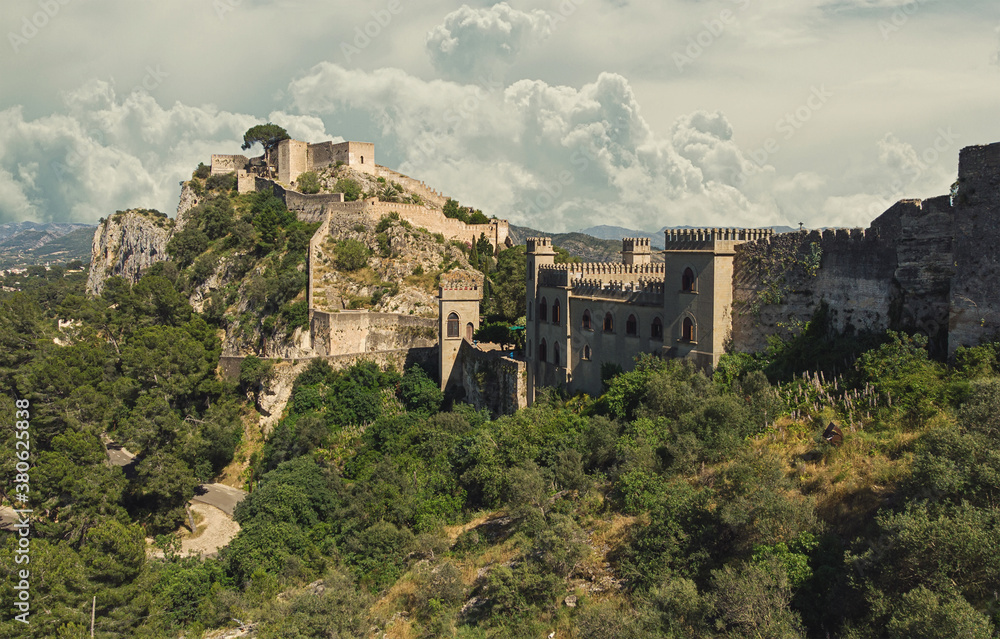 Aerial image picturesque view to ancient famous castle of Xativa against cloudy sky background. Spanish landmark located on hillside top green mountain surrounding countryside. Valencia, Spain