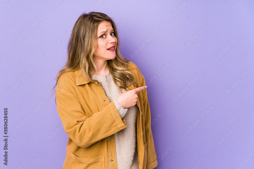 Young caucasian woman isolated on purple background smiling and pointing aside, showing something at blank space. Young caucasian woman isolated on purple background smiling and pointing aside, showing something at blank space.