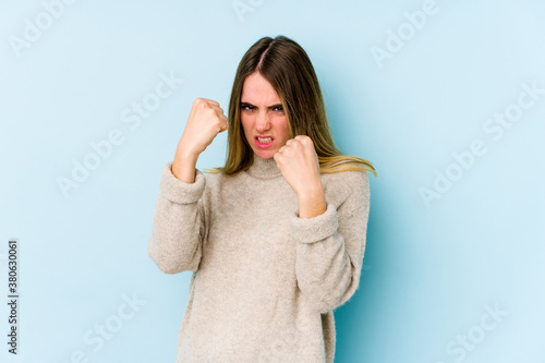 Young caucasian woman isolated on blue background showing fist to camera, aggressive facial expression.