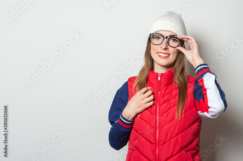 Young woman with a smile in a red vest, hat and glasses on a light background