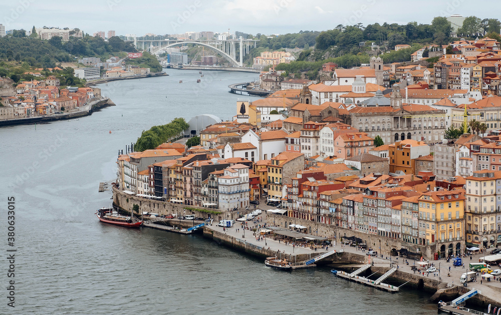 Streets with pedestrians and riverboats on river Douro, cityscape with red tile roofs of historical buildings