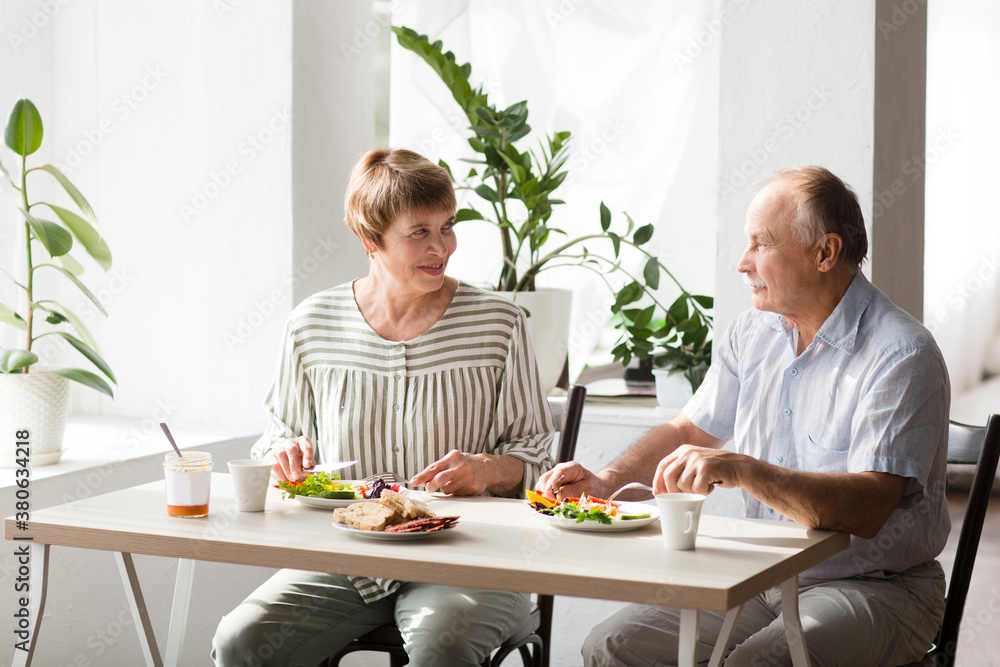 Portrait of relaxed fun senior couple together and eating breakfast in their kitchen at home

