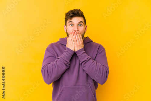 Young caucasian man isolated on yellow background shocked, covering mouth with hands, anxious to discover something new.