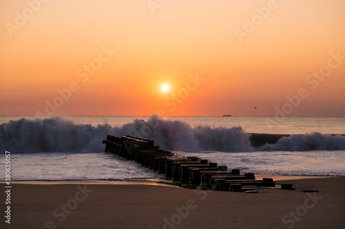 A beautiful sunrise on the last day of Summer at Rehobeth Beach in Delaware. A freight carrying cargo ship is passing by in the distance and the surf is about to role onto the jetty.